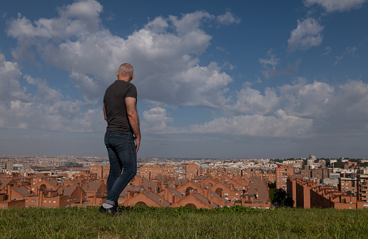 Rear view of adult man standing on grass looking at city view. Madrid, Spain