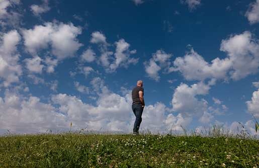 Full length of adult man standing on grass against cloudy sky