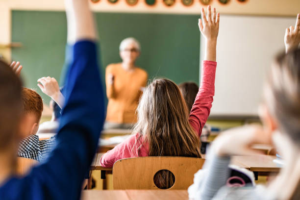istock Back view of students raising their hands to answer the teacher's question on a class. 1401278065
