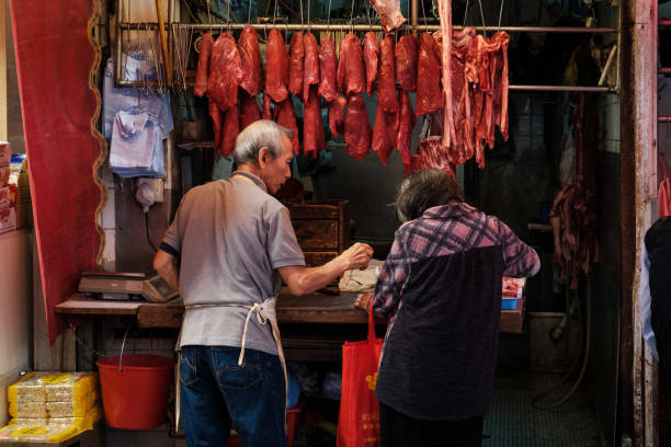 boucher vendant de la viande à une femme âgée dans un magasin du marché de rue à hong kong - butcher butchers shop meat store photos et images de collection