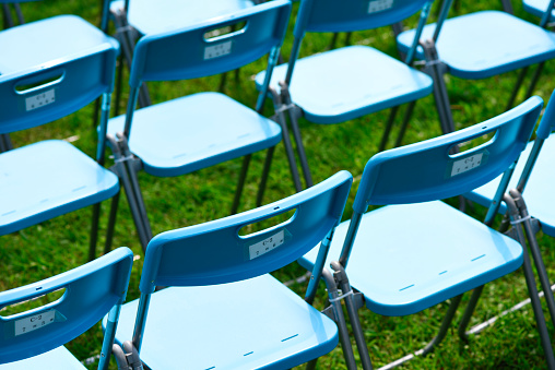 Lots of blue chairs lined up on the park lawn with shallow depth of field.