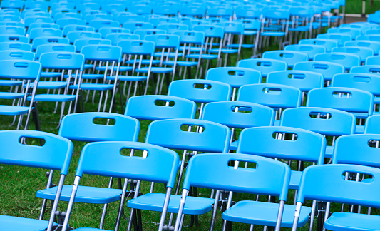 Lots of blue chairs lined up on the park lawn with shallow depth of field.