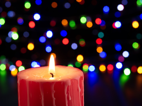 Red Jingle bell glowing in fir tree with Christmas lights on sparkling red background blurred