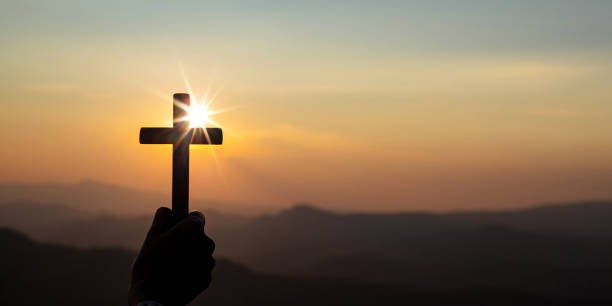 silhouette hand holding cross Banner panorama of human hand holding cross with light sunset background. Christian concept christian social union photos stock pictures, royalty-free photos & images