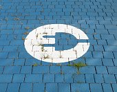 Electric vehicle parking sign  painted on blue tiles. Weeds between the tiled pavement.