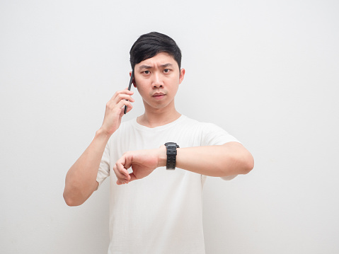 Asian man holding cellphone show his watch up serious face businessman concept
