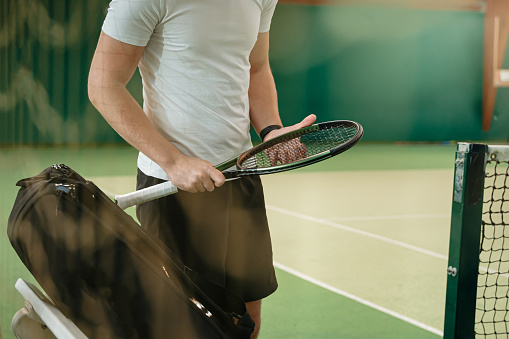 Young male tennis coach checks the quality of tennis racket net at tennis court before practicing