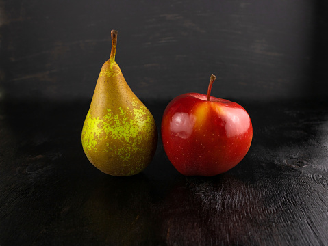 Green pear and red Apple on dark wooden background