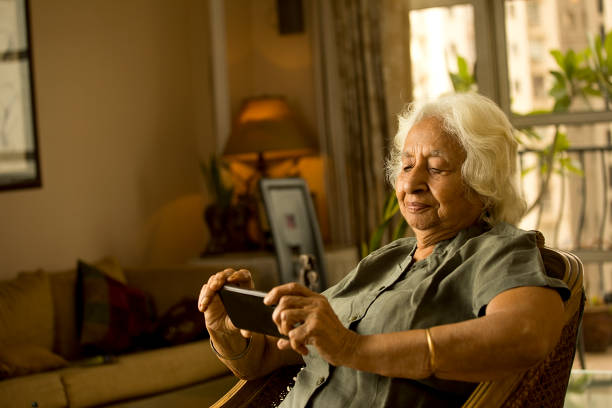 stara kobieta za pomocą telefonu komórkowego w domu - old armchair women senior adult zdjęcia i obrazy z banku zdjęć