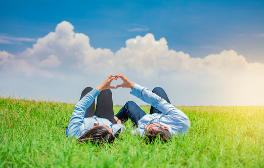 Happy couple lying on grass making heart shape, Couple on grass making heart shape with hands, Young couple lying on grass making love symbol with hands