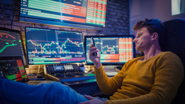 istock Man using mobile phone while monitoring stock market on computer screens at desk 1401290692