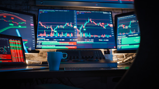 Stock market graphs on computer screens with blue coffee cup on desk at workplace