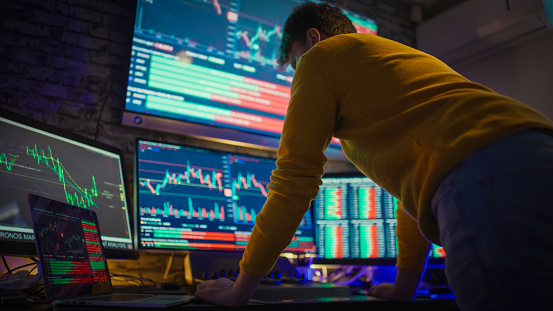 Trader leaning on desk while analyzing stock market reports on computer screens at workplace