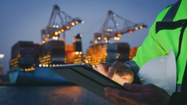 istock Man holding helmet and working on tablet computer in front of harbor terminal at night 1401294482