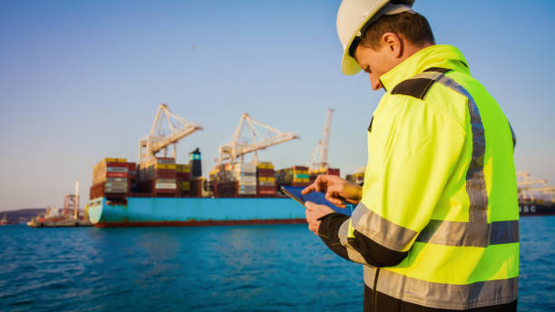 homem em equipamento de proteção trabalhando em tablet em frente ao terminal portuário - industrial ship dock worker engineer harbor - fotografias e filmes do acervo