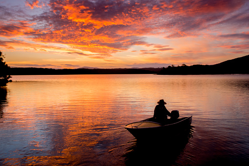 Beautiful sunset on tranquility lake with fishing boat silhouette. Water reflections stunning nature background