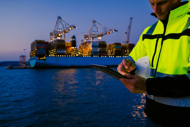 istock Man holding helmet and working on tablet computer in front of harbor terminal at night 1401294794