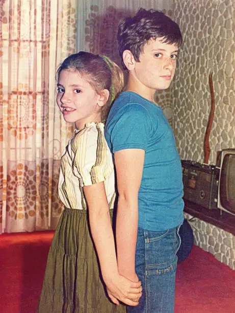 Vintage analog portrait of a pre-teenage boy and a girl posing to the camera at home. Vintage image from the seventies/eighties of the 20th century.