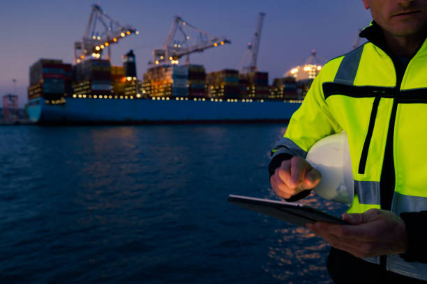 istock Man holding helmet and working on tablet computer in front of harbor terminal at night 1401295669