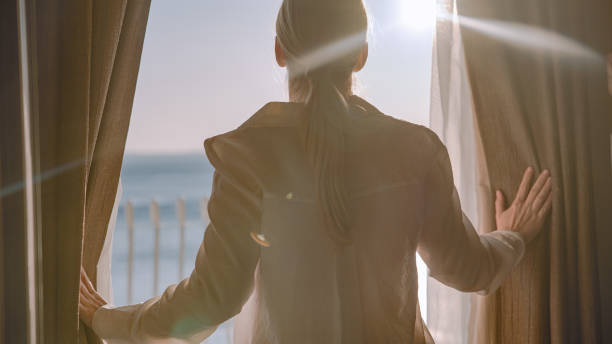 istock Woman opens window curtains on sea view window 1401297423