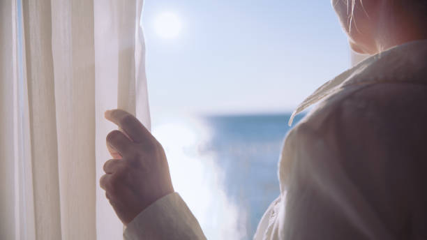 Woman opens window curtain on sea view window