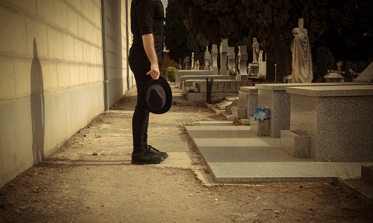 Adult man in black holding hat mourning in cemetery