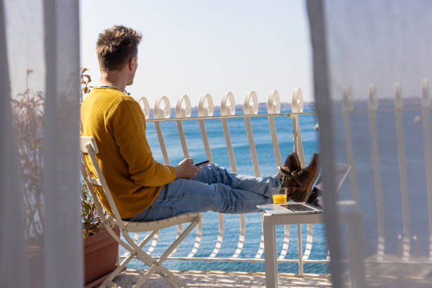 istock Man enjoying sea view while sitting beside laptop on hotel balcony 1401303178