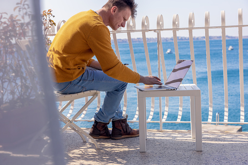 Man sitting on chair using laptop on modern hotel balcony