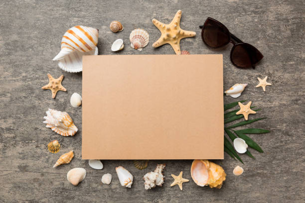 istock Summer time concept with blank greeting card and blank craft paper on colored background. Seashells from ocean shore in the shape of frame separated with space for text top view 1401304393