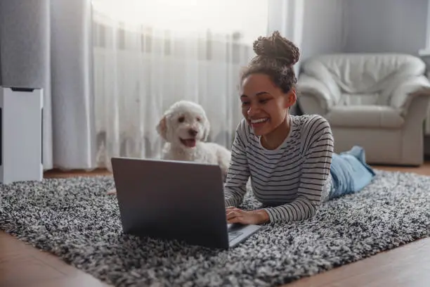Photo of Happy positive female searching internet on laptop computer at cozy house on carpet
