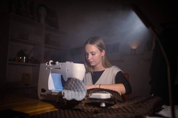 Young woman stitching a designer dress on sewing machine at her atelier late in the night