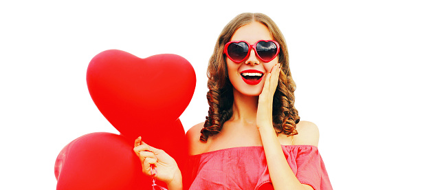 Portrait of happy surprised laughing young woman with red heart shaped balloons wearing sunglasses isolated on white background