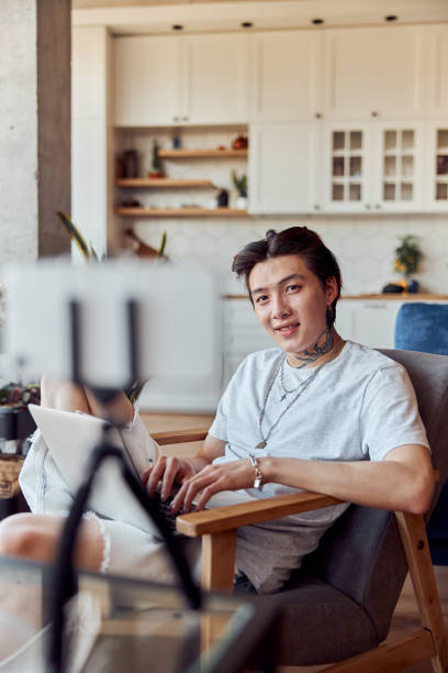 istock Happy male Asian vlogger working at home while using laptop and typing 1401309459