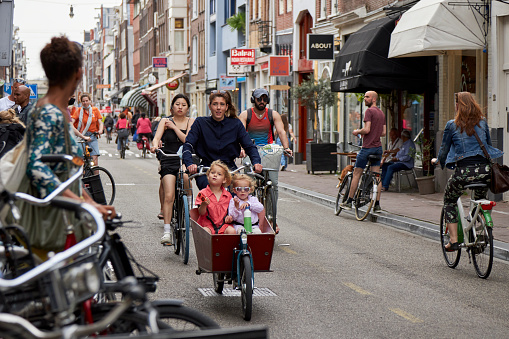 Shopping street with woman on Dutch cargo bike at summer sunset, Haarlemmerdijk, Amsterdam, The Netherlands.