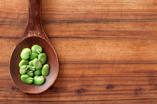 Top view of wooden spoon over table with boiled broad beans on it