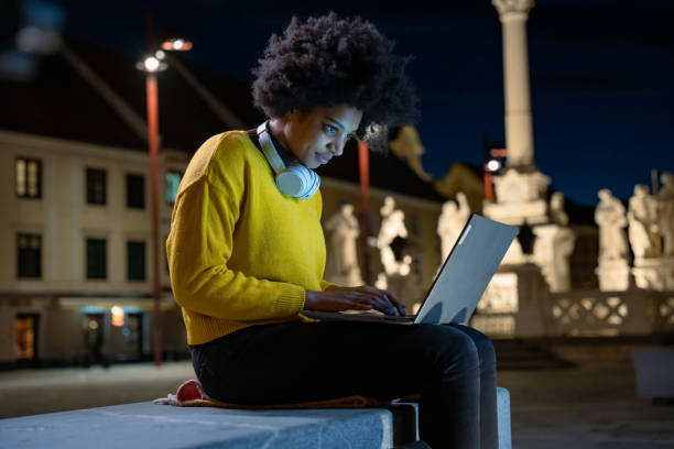 istock Young woman working on laptop while sitting on bench in city 1401311557