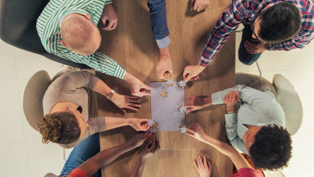 istock Diverse group of friends sitting around table, solving a jigsaw puzzle together 1401318317