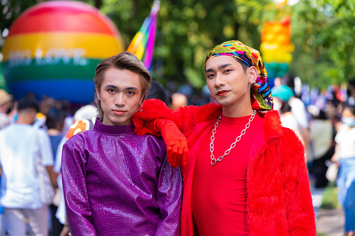 Asian young gay couple embracing and showing their love with rainbow flag at the street.