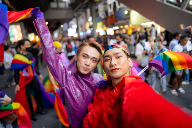gay asian couple smiling and taking a selfie enjoying  pride parade. - stereotypical imagens e fotografias de stock