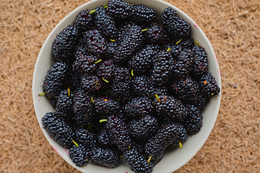 Ripe mulberry berries in a ceramic plate, top view, seasonal summer berry.