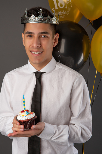 Smiling handsome mixed race man celebrating his birthday with cupcake and balloons.