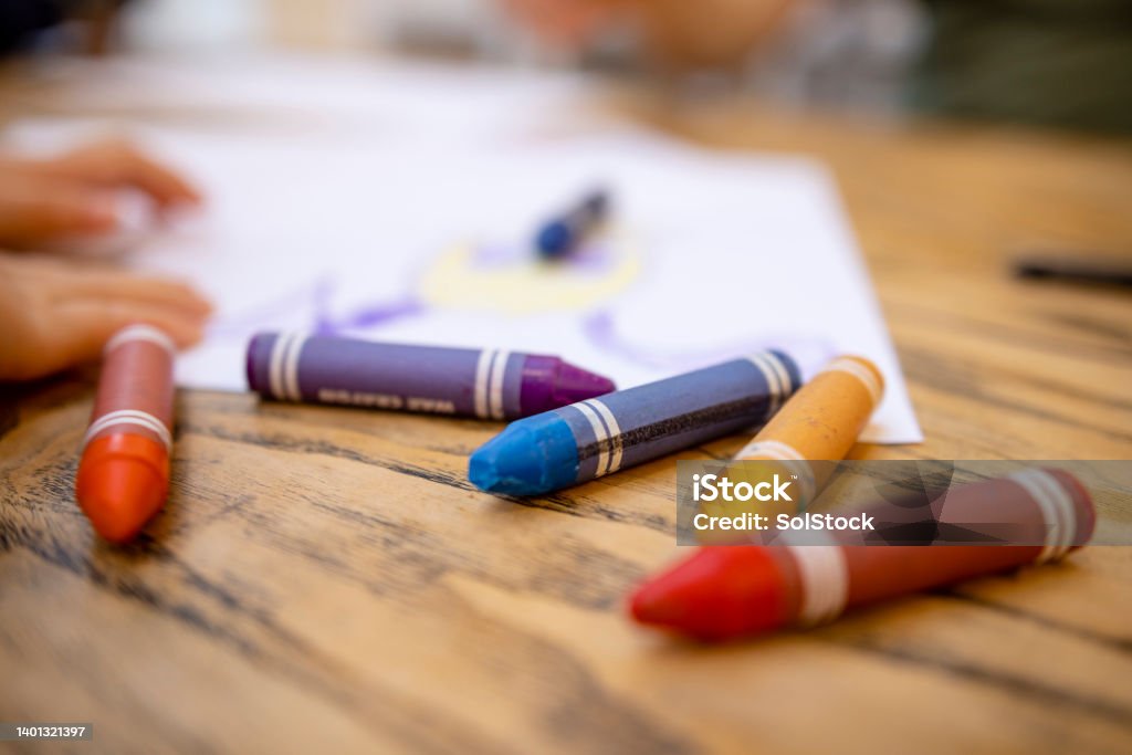 Colourful Crayons on Table A close-up shot of colourful crayons on a wooden table with paper. Child Care Stock Photo