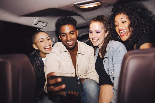 Happy friends taking a selfie together inside a car at night. Group of young friends smiling cheerfully while posing for a group photo. Carefree friends taking a ride home after a party.