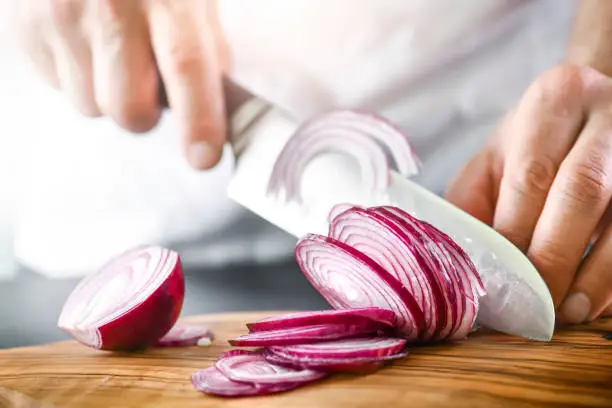 Man hands cutting red fresh onion with knife.