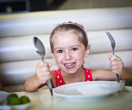 Cheerful little girl waiting for her meal in the restaurant