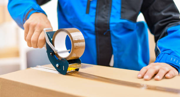 Worker hands holding packing machine and sealing cardboard or paper boxes stock photo