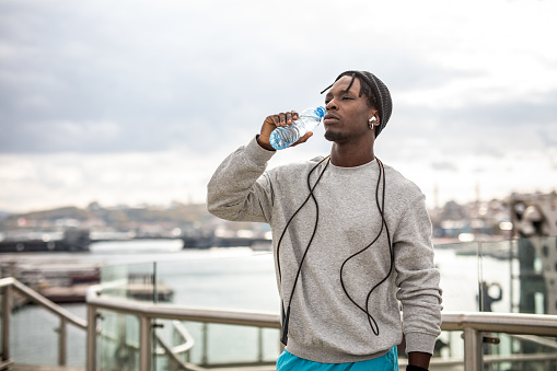 One black man, an athlete, drinks water from a bottle after training outdoors.