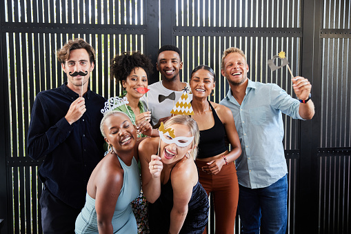 Portrait of a laughing group of diverse young people posing together with photo booth accessories during a party at a friend's home