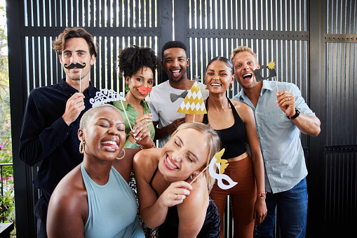Portrait of a diverse group of laughing young people posing together with photo booth accessories during a party at a friend's home