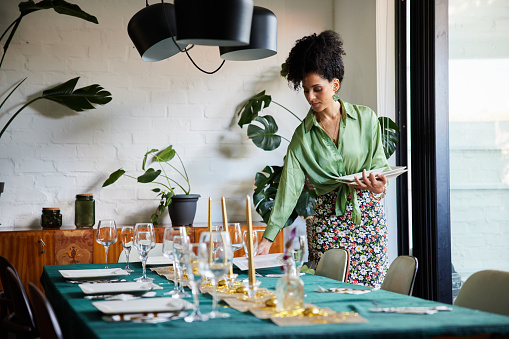 Young woman setting plates on her dining room table at home before a dinner party for friends